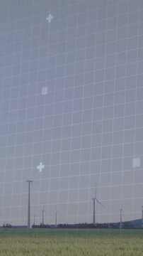 Vertical video: On data feed, grid and code overlay pulsing above wind turbines monitoring power