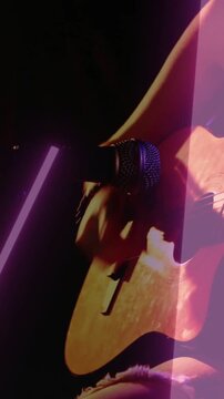 Vertical video: Player bringing mic to hole, performing, causing zoom, strumming, neon-lit guitar