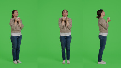 Obraz premium Caucasian girl drinking cup of coffee over full body greenscreen background, holding caffeine drink in studio. Young woman enjoying caffeine beverage on isolated greenscreen, portrait.