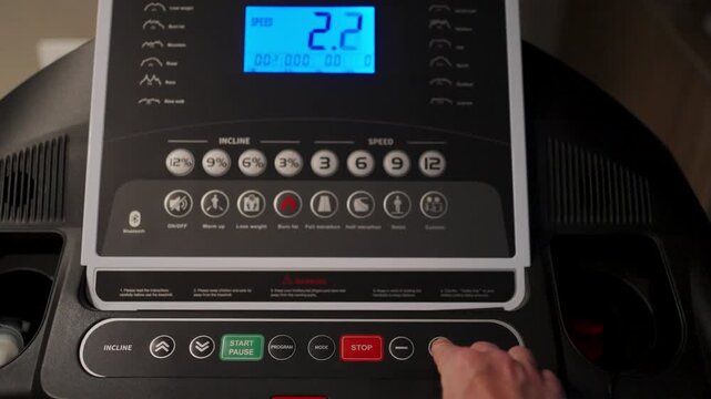 Man Hand Pressing Button on Treadmill Control Panel. Close-up of a person starting a workout by pressing a button on a treadmill dashboard. Modern cardio equipment in a home gym