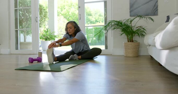 African American woman starting leg out reaching on green mat holding toes stretching hamstring