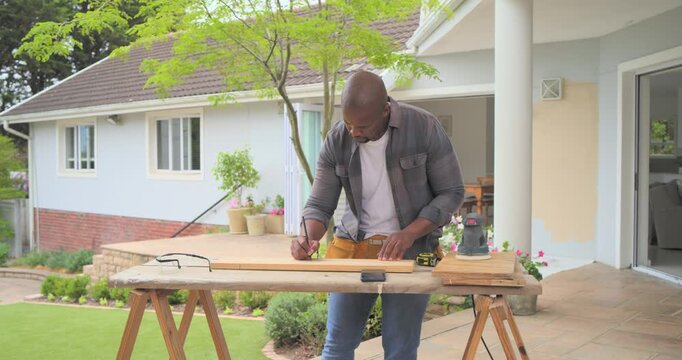 Man measuring with tape measure and sanding board on covered patio workbench using orbital sander