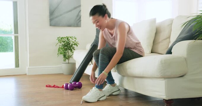 African American woman on couch tying sneakers, preparing for home workout in pink top near mat