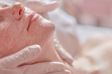 Naklejka premium Woman receiving facial treatment with hands applying skincare product