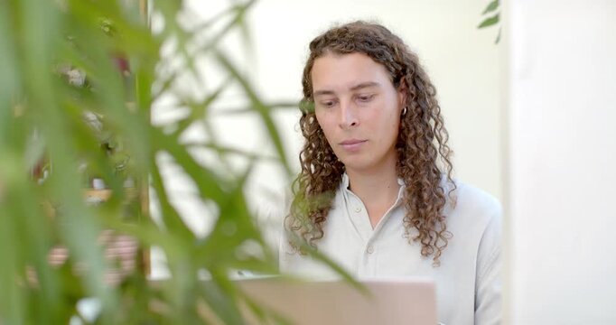Non-binary person sitting at desk reading laptop, taking notes with pen for work while plant moving