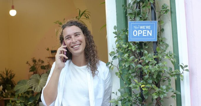 Nonbinary African adult answering shop call, checking pink-case phone, standing by open sign