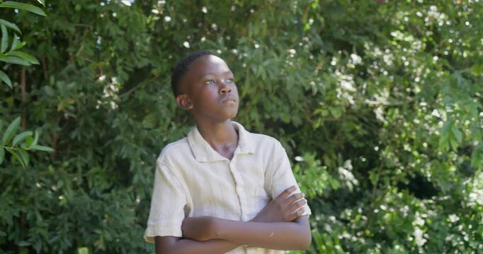 African male youth in beige shirt reacting to camera move uncrossing arms, turning, smiling in yard