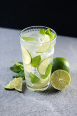 Fototapeta premium Fresh mojito cocktail with lime, mint and ice in glass on gray surface and black background. 