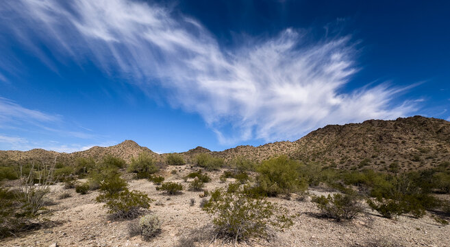 Wispy cirrus clouds dance over the rugged Sonoran Desert, where scrubby desert brush and rocky hillsides tell the story of a land both harsh and beautiful.