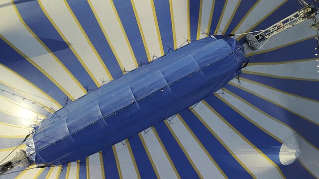 Aerial view of expansive circus tents with alternating blue and white stripes, creating a striking contrast against the dark asphalt ground, St. Augustine, Florida, United States.