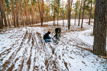Naklejka premium Two Young Men Preparing and Repairing BMX Bikes on a Snowy Path in a Pine Forest During Winter