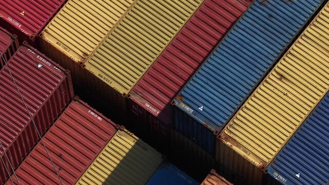 Aerial view of shipping containers stacked in neat rows, displaying a colourful palette of red, yellow and blue hues, Setubal, Portugal.