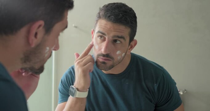 Adult man leaning at mirror checking skin for care dabbing cream rubbing at vanity
