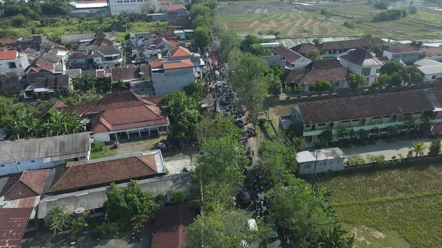 Aerial view of a busy village street with houses and rice fields in Indonesia, 4K footage.