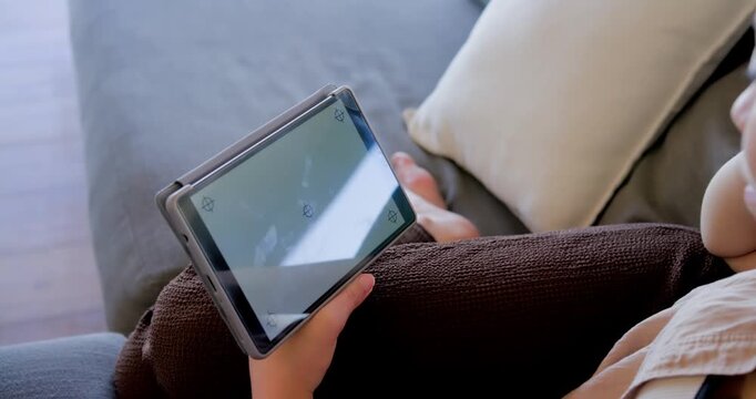 African American woman holding tablet on couch, tapping corner markers while tilting to avoid glare