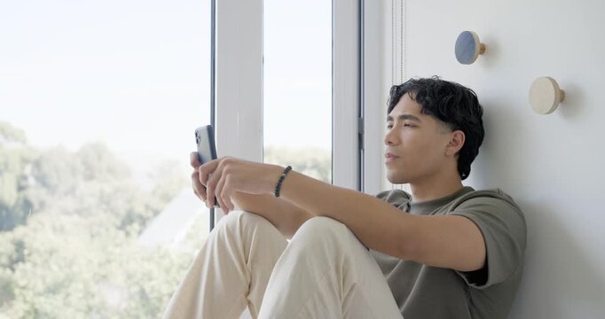 Music starting, man sitting by narrow window, holding phone, glancing and singing along