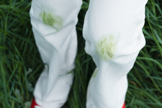 Close up of dirty stains on green grass during summer activities in the park outdoors. The individual is wearing red shoes and is outside near trees. Concept of daily stains on clothes.