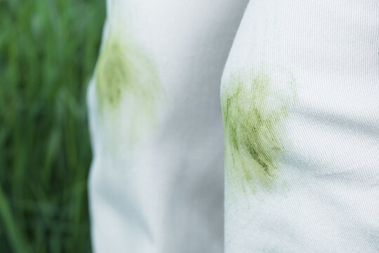 Close up of dirty stains on green grass during summer activities in the park outdoors. The individual is wearing red shoes and is outside near trees. Concept of daily stains on clothes.