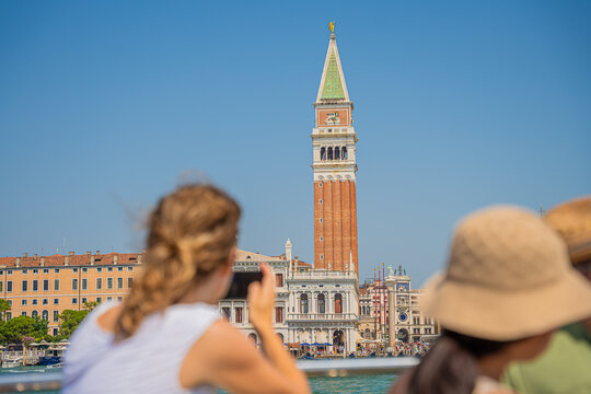Venice, Italy - 29 March 2026: View of the iconic St. Mark's Campanile rising majestically against the clear blue sky, framed by blurred figures and historic buildings.