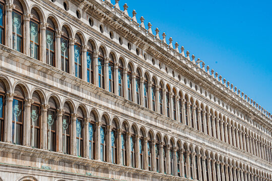 Venice, Italy - 29 March 2026: View of the Procuratie Vecchie's ornate facade, a symphony of arched windows and decorative stonework against a clear blue sky.