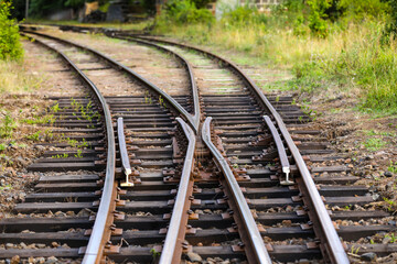 Fototapeta premium Railroad turnout switch with converging and diverging rails on weathered ties and gravel, evoking choices, crossroads, change and a journey toward different futures