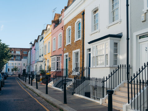 London, United Kingdom - 21 June 2025: View of a row of terraced houses displaying pastel hues and vibrant colors, their facades catching the warm sunlight along the quiet street.