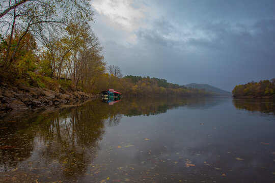 View of still waters reflecting the muted autumn foliage and an anchored houseboat under a brooding sky, Little Rock, Arkansas, United States.