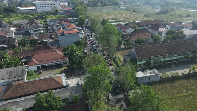 Aerial view of a busy village street with houses and rice fields in Indonesia, 4K footage.