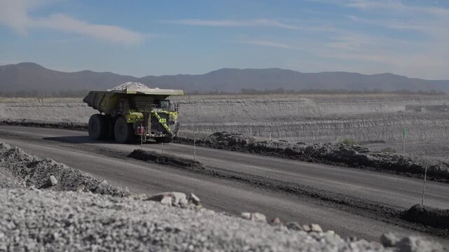 Massive mining haul truck carrying overburden along haul road in open-cut coal mine. Industrial resource extraction, heavy machinery, and large-scale earthworks in remote landscape.