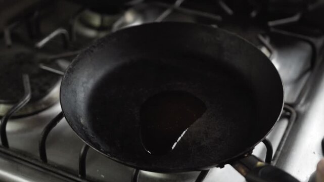 Closeup of oil spreading and heating in pan on stove showing cooking preparation step and heat process in kitchen