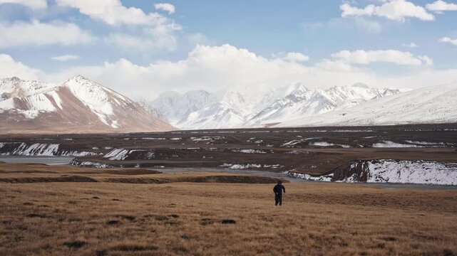 Joyful male tourist freedom running toward Tian Shan mountain on autumn grassland in Sary Jaz Valley