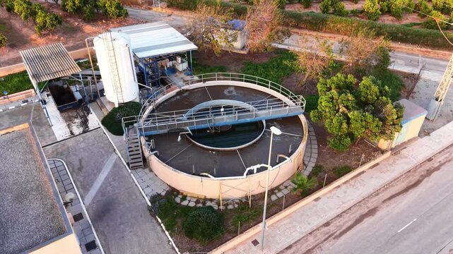 Compact wastewater treatment plant with circular clarifier tank, outer aeration ring, walkway bridge, and mechanical equipment surrounded by greenery