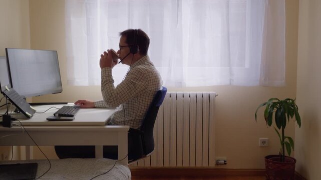 Man drinking coffee and taking notes while teleworking