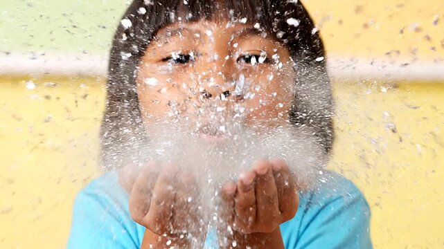 Close-up of a young child blowing glitter from their hands, creating a sparkling cloud against a colorful background