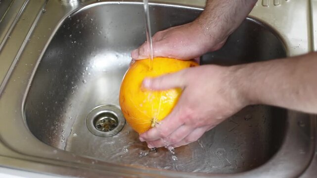 Washing melons in close-up under the tap of running water in the sink