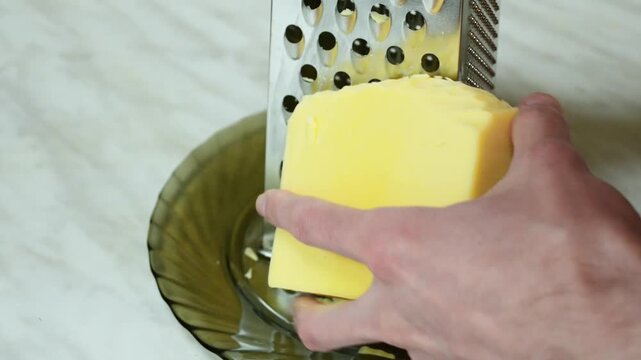 Process of grating cheese on a red grater over a bowl in the kitchen.