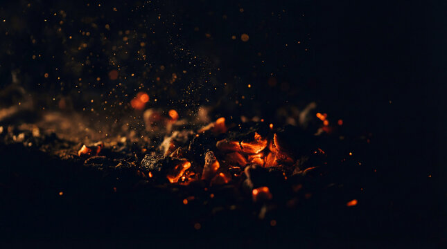 Close-up of glowing embers and ash scattered against a dark background, representing heat and destruction.