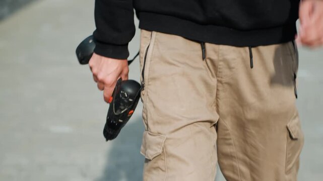 White man strides holding drill on city sidewalk, tan cargo pants and black sweater, closeup on hand and tool, contractor heading to jobsite, focused practical mood with daylight highlights and soft