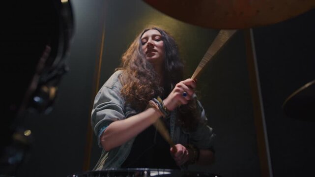 Woman drummer plays a drum kit, drumstick. Female musician beats a rock rhythm on drums, cymbals. Girl artist is rehearsing in a room or performing on festival stage. Alternative indie band in club