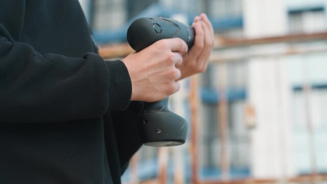 Closeup hands testing drill power and speed, outdoor balcony scene with urban building backdrop, steady finger on trigger and firm grip, final check before fastening and finishing construction or DIY