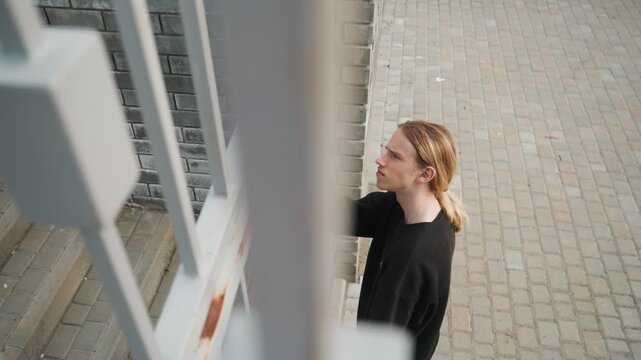 White man at building intercom pressing buzzer on cobblestone pavement casual young adult in black sweater with ponytail captured from overhead angle sequential frames show approach, reach, press,