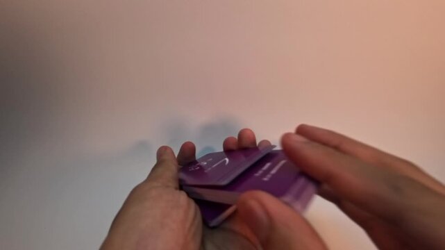 Close-up of hands expertly shuffling a deck of purple Hiragana language flashcards against a neutral background.