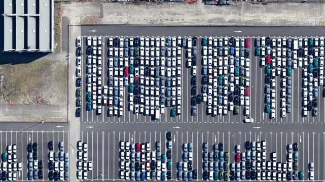 Aerial view of a large parking lot filled with tightly packed cars, a geometric tapestry of whites, greens, blues, and reds, Sausheim, Grand Est, France.