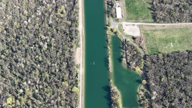 Aerial view of a long canal cutting through lush forests, with hints of buildings and roads nearby, creating a blend of nature and infrastructure, Sausheim, Grand Est, France.