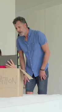 Vertical video: Packing man in blue shirt and shorts filling DONATION box on bed, checking tablet