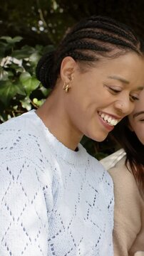Vertical video: Turning woman with braids laughing as friend approaches in garden in blue sweater