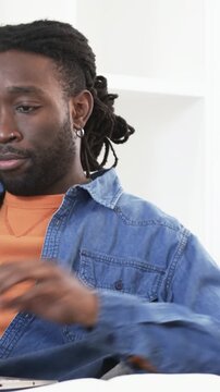 Vertical video: Finishing sip, man in denim typing on laptop at desk, with mug and open notebook
