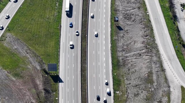 Aerial view of a busy highway with cars and trucks, juxtaposed against green patches and bare earth, creating a dynamic scene, Sausheim, Grand Est, France.