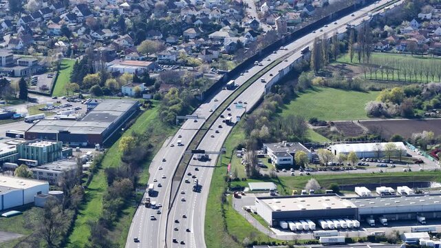 Aerial view of a highway cutting through buildings and green spaces, a contrast of urban infrastructure and nature, Sausheim, Grand Est, France.