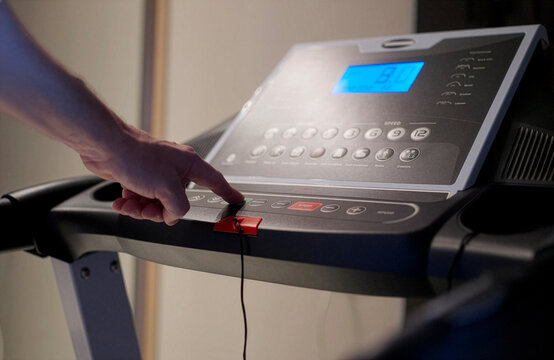 Man Hand Pressing Button on Treadmill Control Panel. Close-up of a person starting a workout by pressing a button on a treadmill dashboard. Modern cardio equipment in a home gym